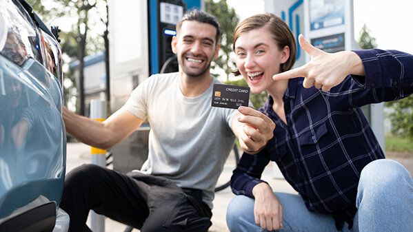 Young couple holding black credit card an electric car charging station.