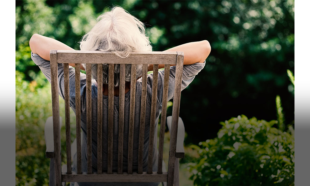 The image shows a woman sitting on a chair in nature.