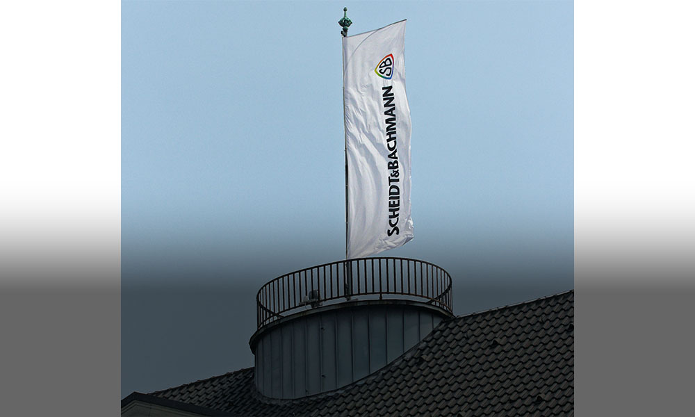 The picture shows a flag with the Scheidt & Bachmann logo on the roof of a house.
