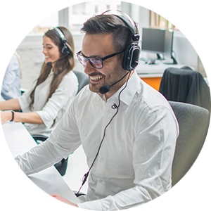 The picture shows friendly smiling service staff in an office at a computer with a headset on.