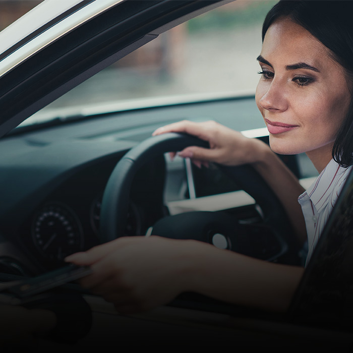 Das Bild zeigt eine Frau in einem Auto, die mit ihrer Hand durch das Fenster nach etwas greift.